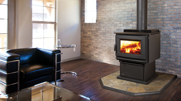 Regency Classic™ F5100 Extra Large Wood Stove with brick wall in background several windows and a black and stainless steel chair